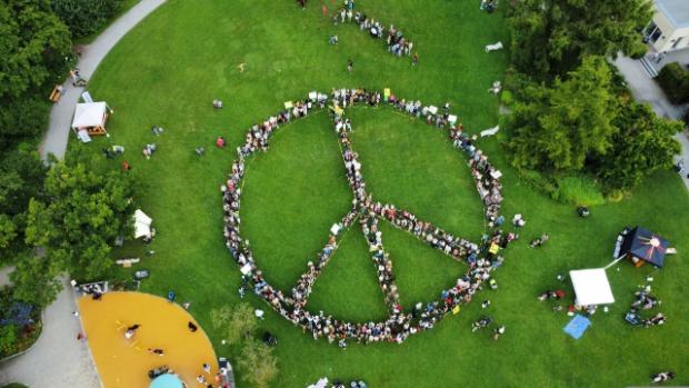 Aufnahme eines aus Menschen gebildeten Peace-Zeichens auf einer grünen Wiese. 